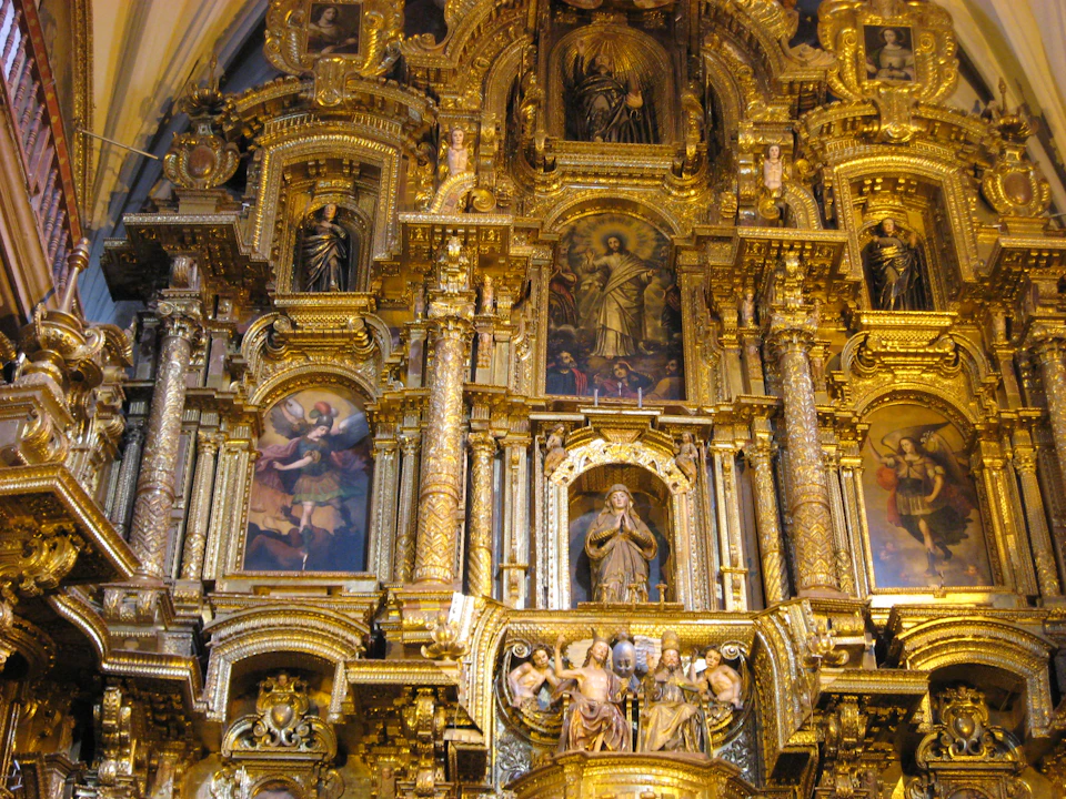 An ornate, gilded altar featuring religious statues and framed paintings, with intricate gold details and columns.