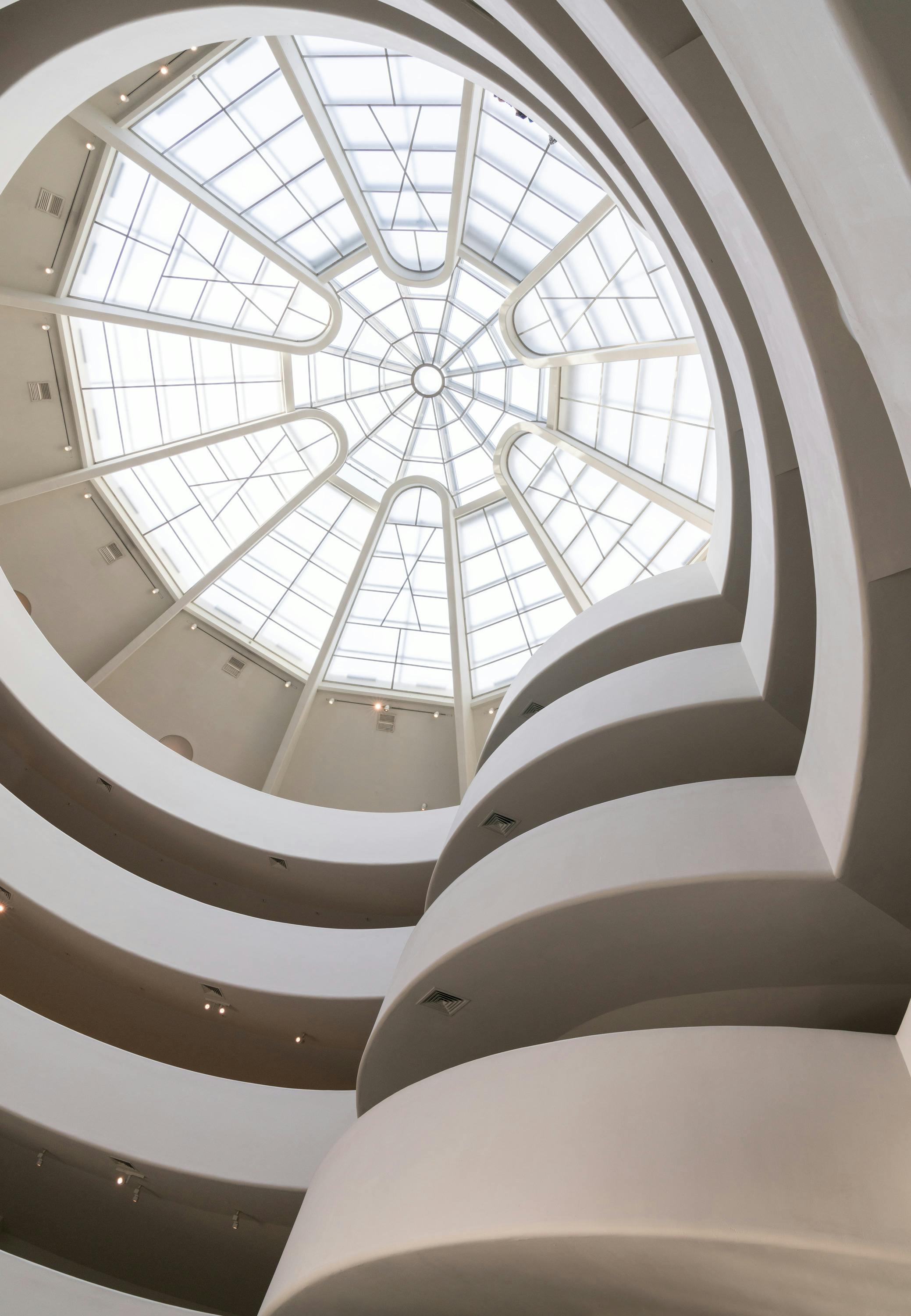 Large skylight with a geometric pattern above multi-level curved walkways, inside a spacious, modern building.