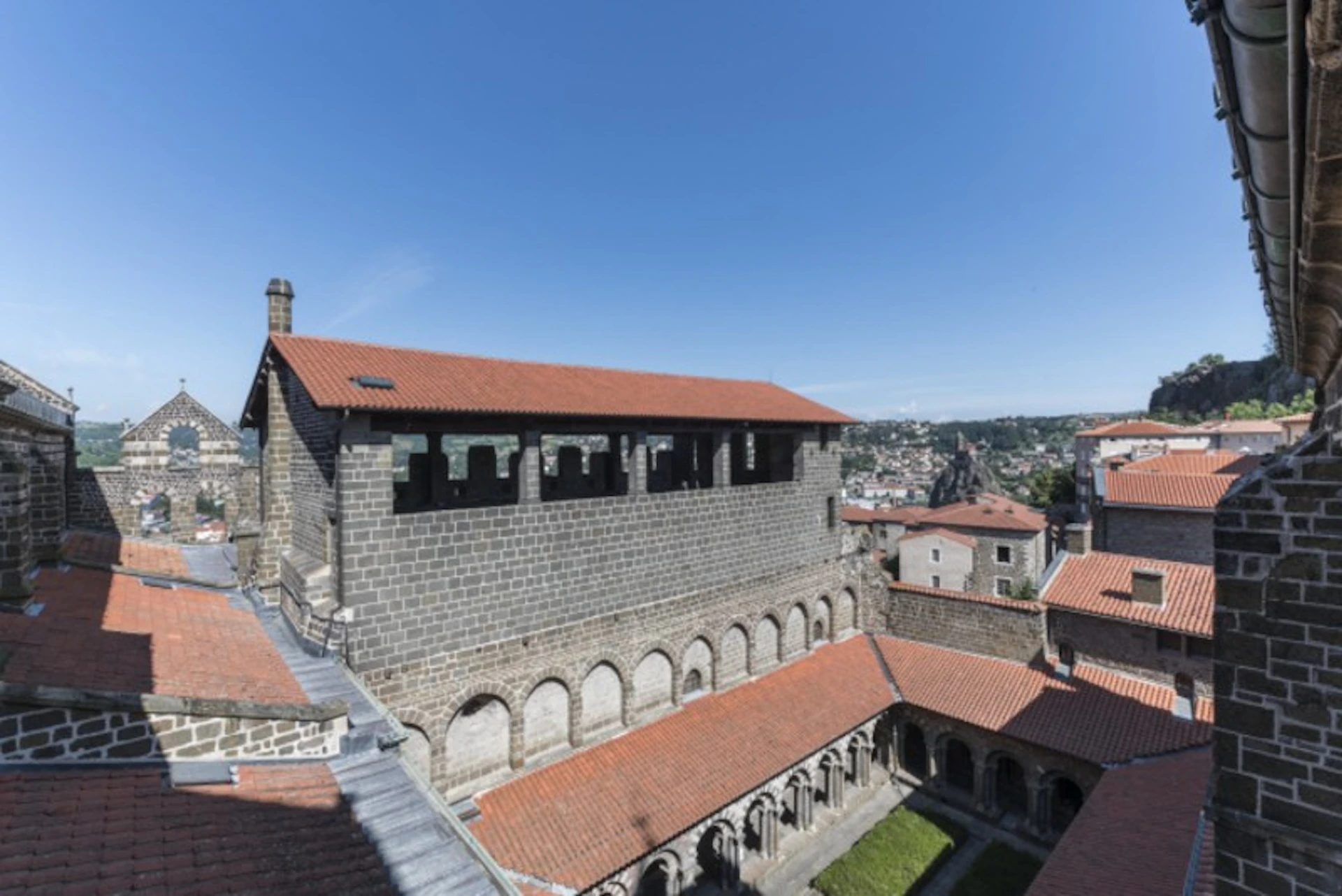A historic stone building with red-tiled roofs, arched windows, and a courtyard, set against a clear blue sky.