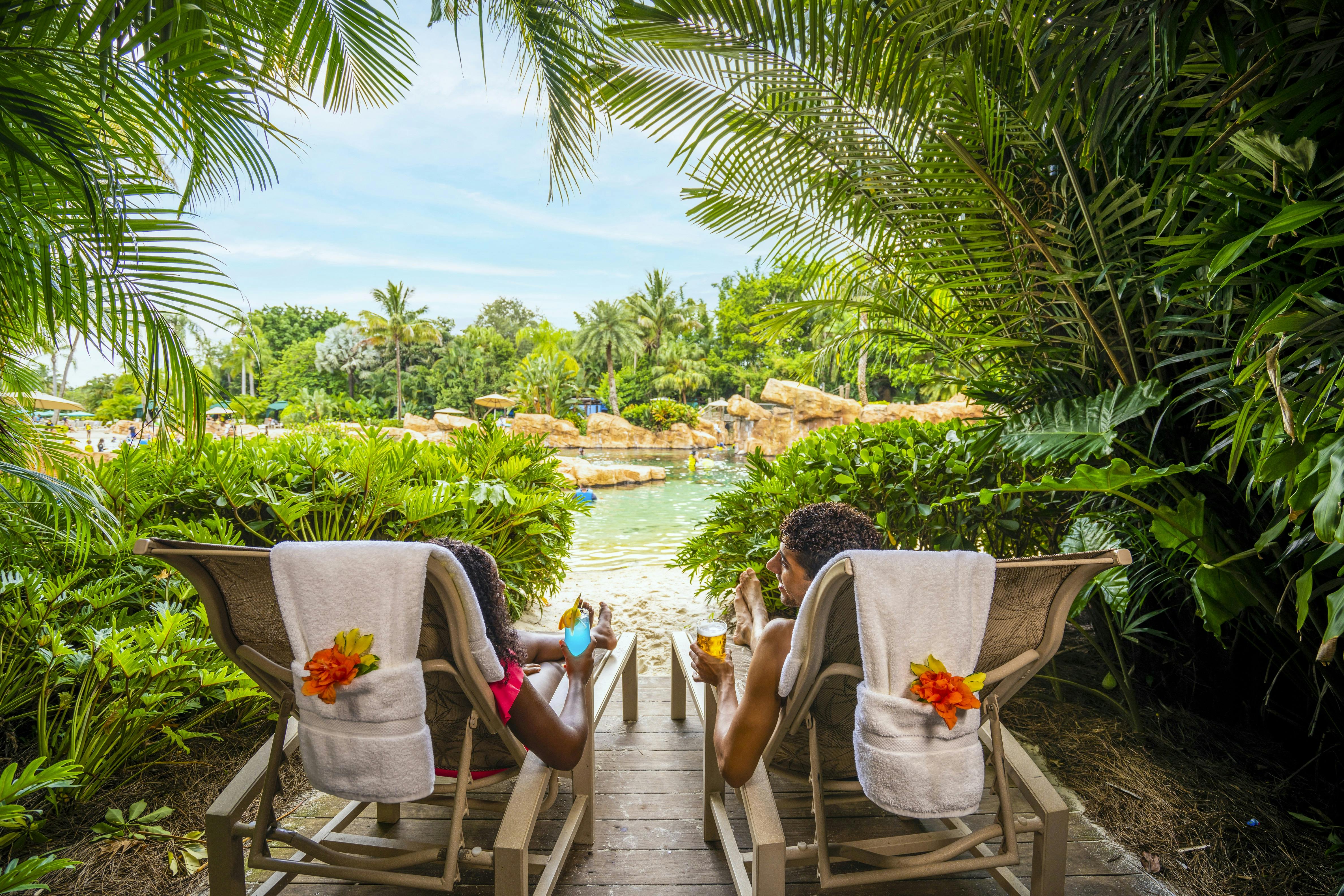 南国の植物に囲まれた椅子に座り、岩と水のある緑豊かな景色を眺めながら、2人でくつろいでいます。