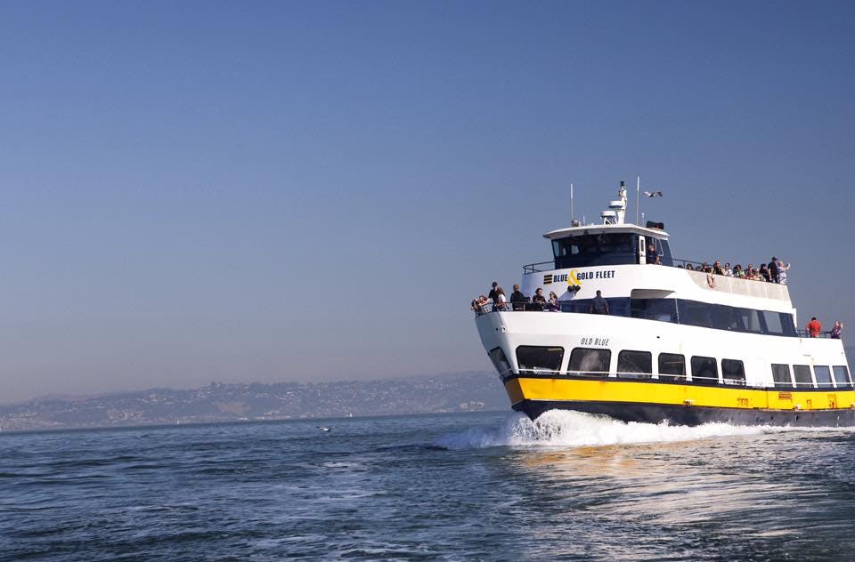 A ferry named "OCD Blue" with passengers on deck sails through the water with a distant coastline under a clear blue sky.