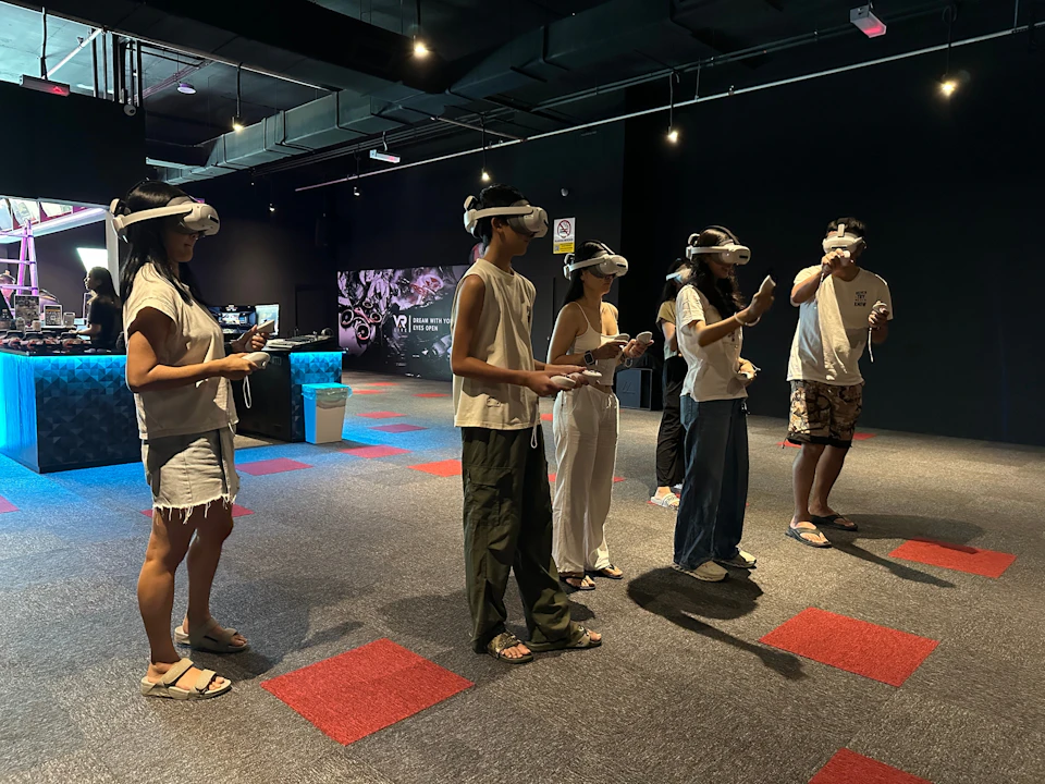 A group of people wearing VR headsets and holding controllers in a dark indoor space with colorful carpet tiles.