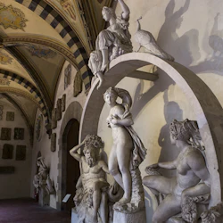 En utsmyckad hall med detaljerade fresker med klassiska statyer, inklusive en naken figur, en sittande man och en påfågel ovanpå en båge.