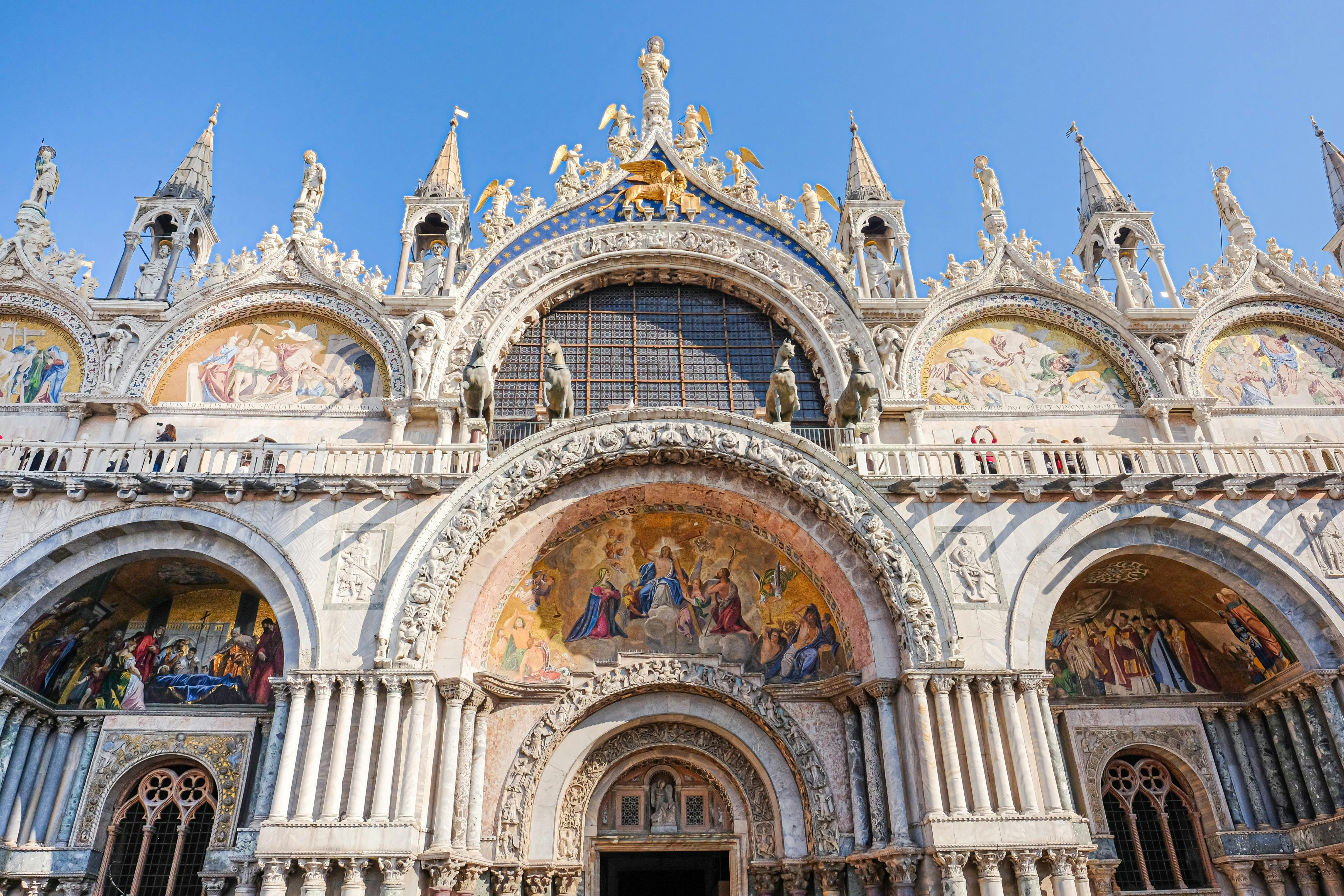 Elaborate cathedral facade with ornate arches, detailed sculptures, and colorful mosaics under a clear blue sky.