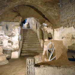 Forntida stentrappa leder till en välvd entré, omgiven av vittrade, sönderfallande väggar och utspridda murverk.