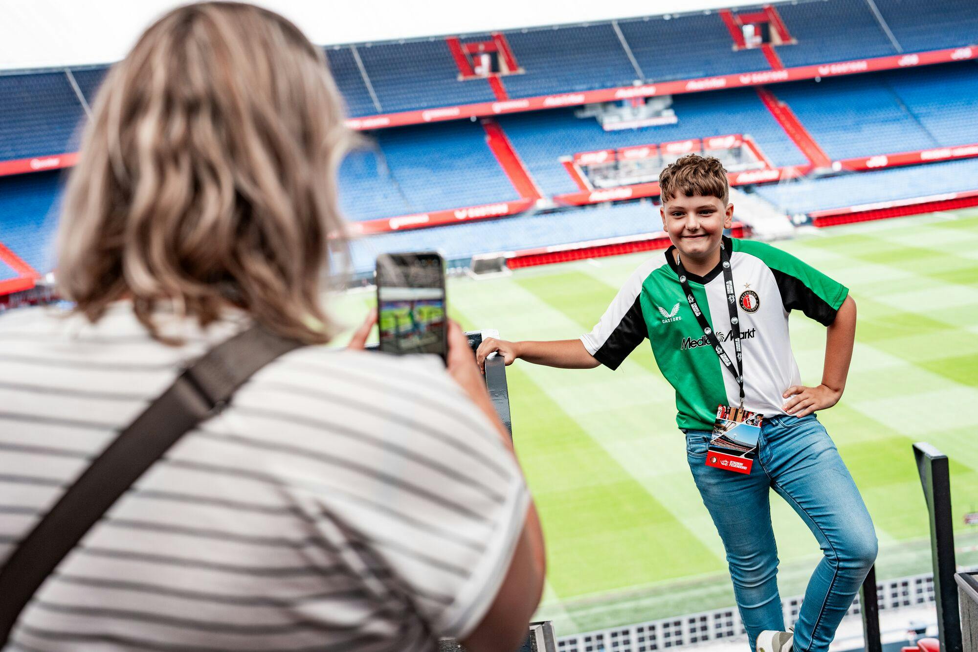 一名男孩穿着绿色和白色的运动衫，在体育场内摆姿势拍照，体育场内有明显的场地和座位部分。