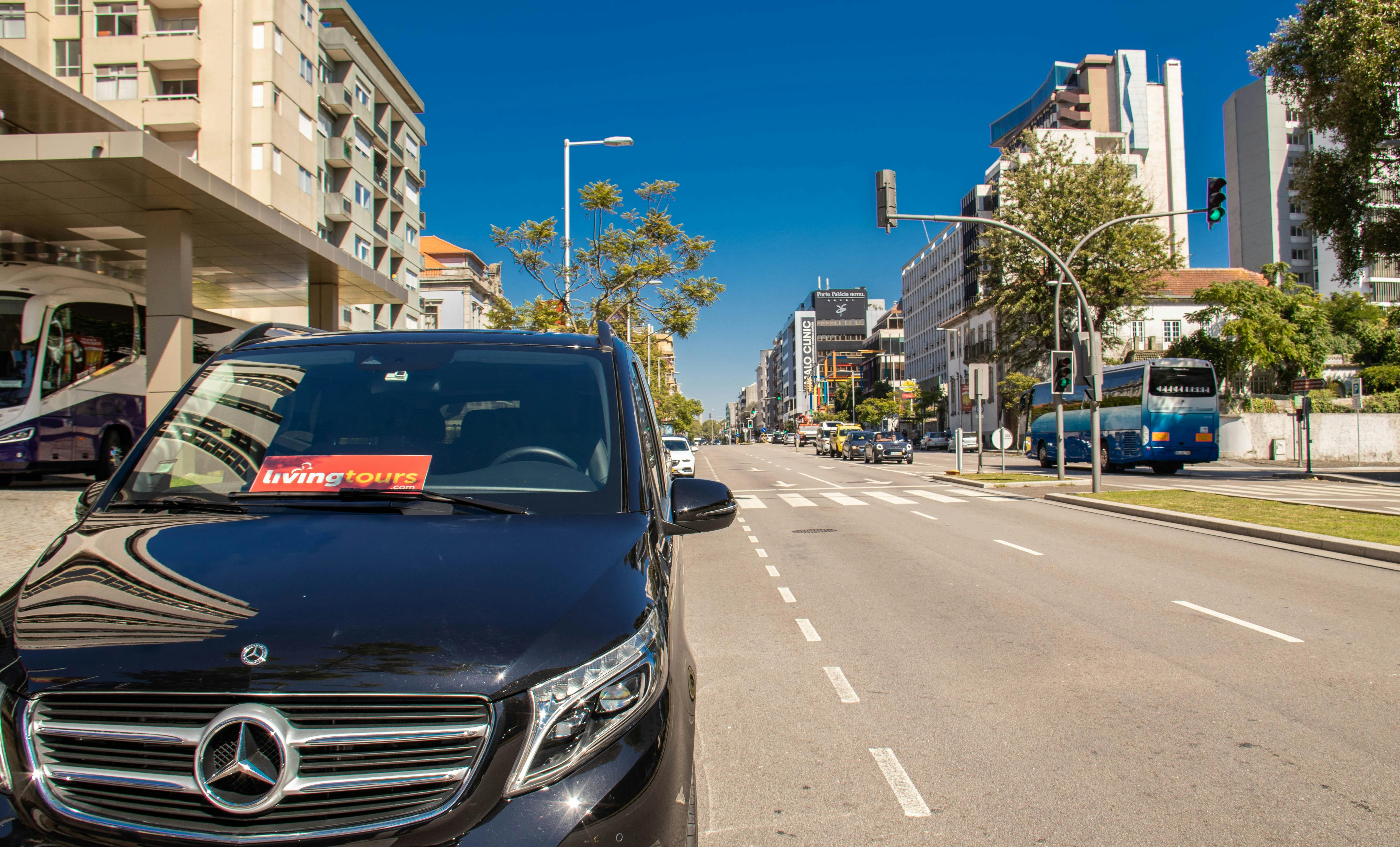 A black van with a "Driving Tours" sign parked on a wide, sunny city street lined with buildings and trees.