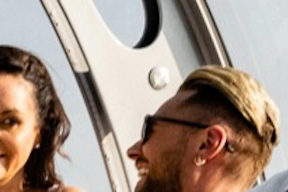 A group of people standing and talking inside a glass-enclosed observation pod with a view of the sea and coastline.