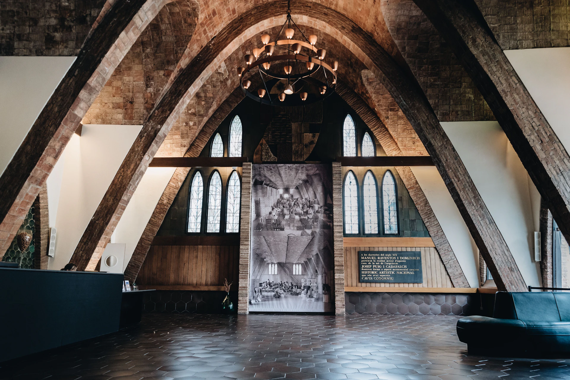 Interior of a church-like structure with arched ceilings, stained glass windows, and a large black-and-white tapestry.