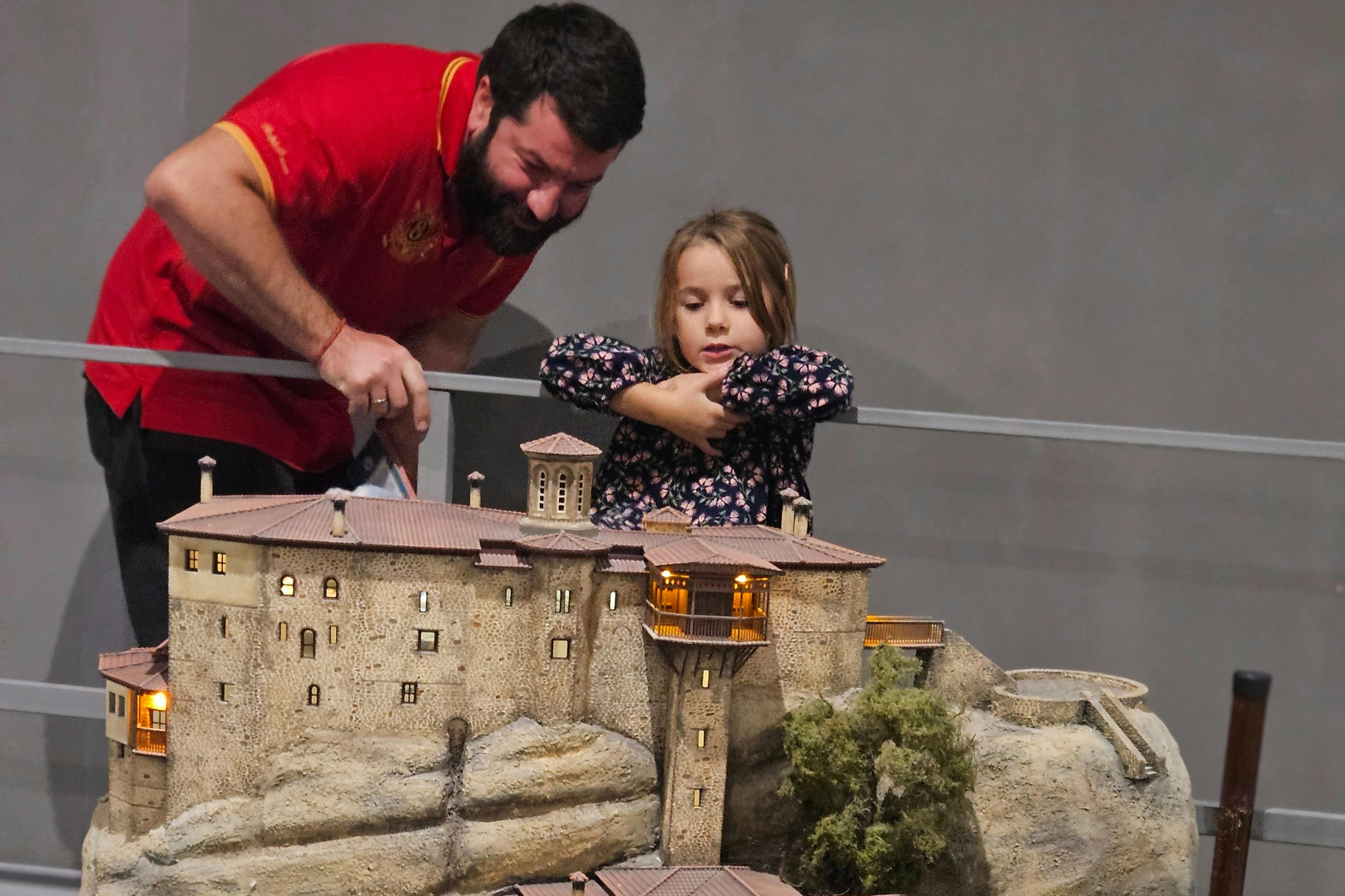 ひげを生やした男性と少女は、岩場にある古代の建物の詳細なミニチュアモデルを見ています。