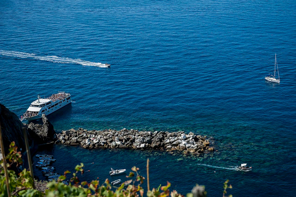 Speedboats on the blue ocean near a rocky breakwater, viewed from above with some foliage in the foreground.