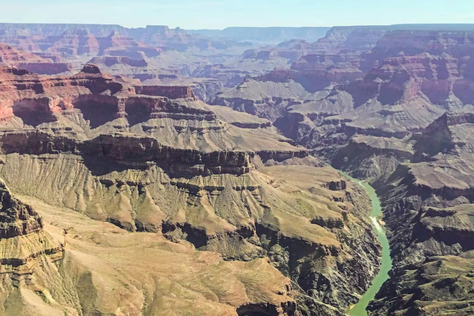 A scenic view of the Grand Canyon with steep cliffs, layered rock formations, and a river winding through the gorge.
