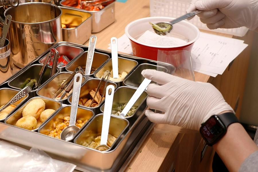 A person wearing gloves prepares food using various ingredients in small containers on a counter.