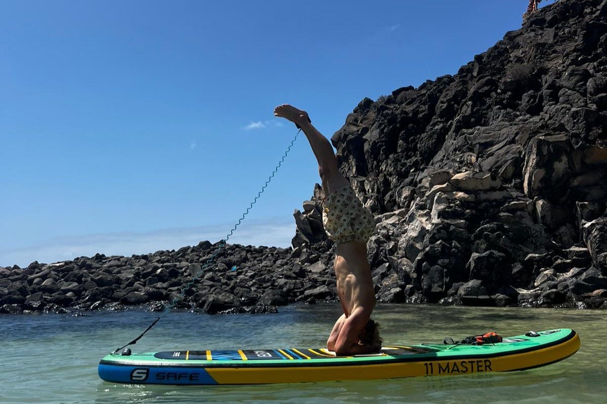 在晴朗的蓝天下，在岩石海岸附近的平静水域中在桨板上执行头架的人。