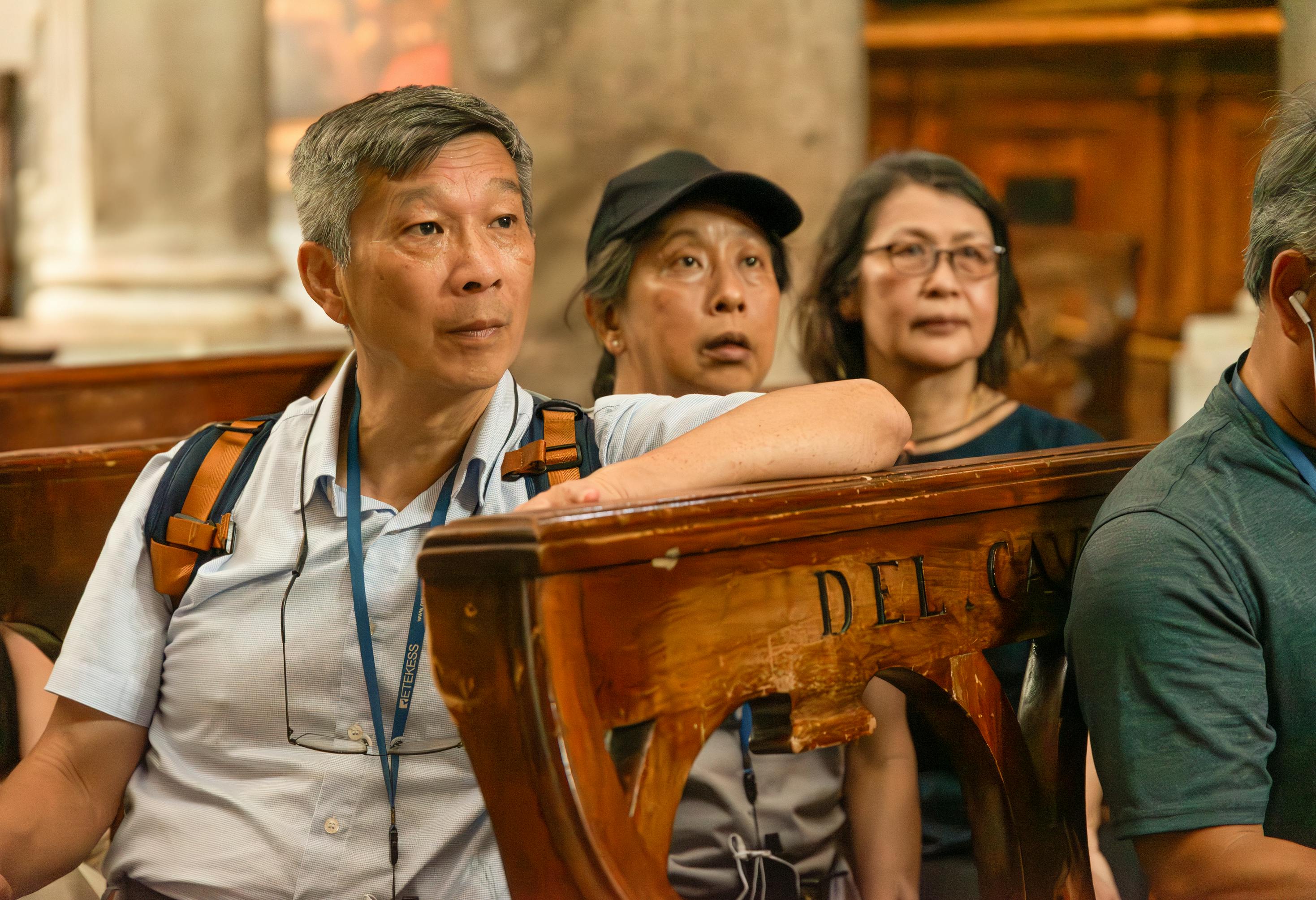 歴史的な石造りの建物と観光客のグループを背景に、草の上に立っている人々。 二人の人物が目の前にいて、空を見上げている。