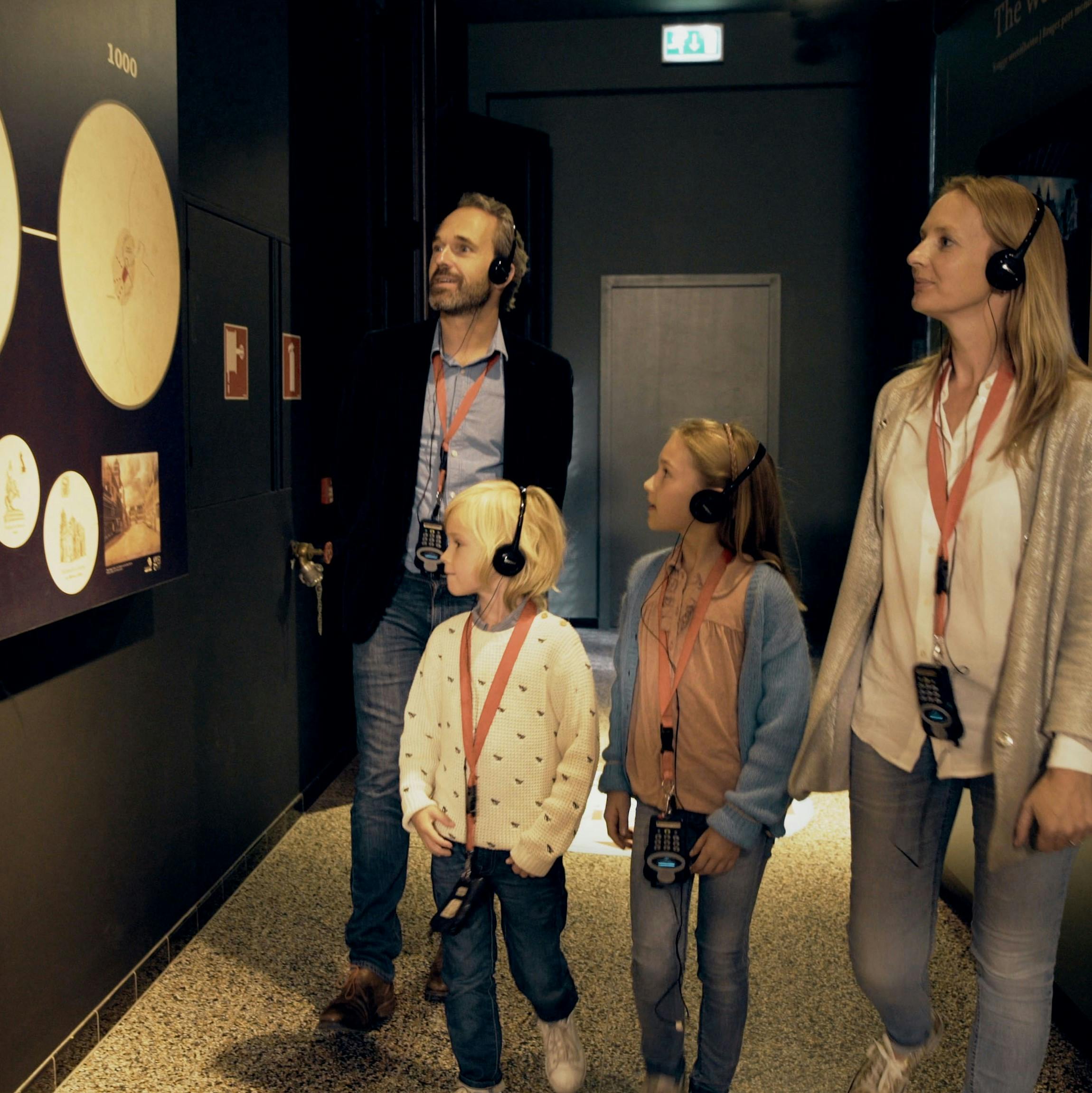 Čtyřčlenná rodina se sluchátky na uších pozoruje exponáty na temné zdi muzea.