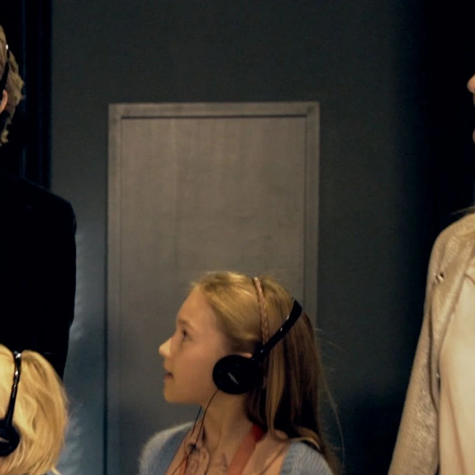 A family of four, wearing headphones, observes exhibits on a dark museum wall.