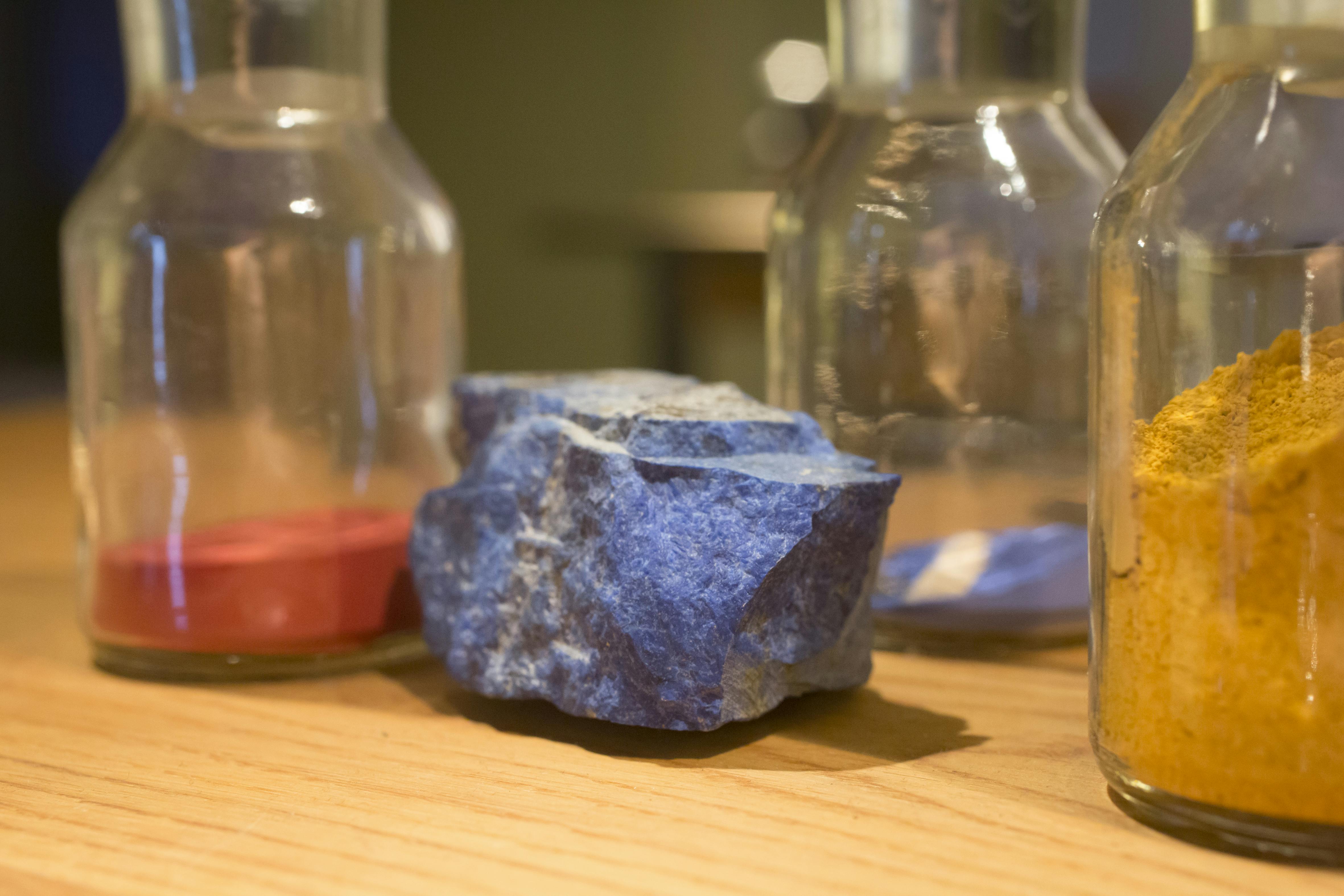 Uma pedra azul rugosa colocada numa superfície de madeira rodeada por três garrafas de vidro transparente.