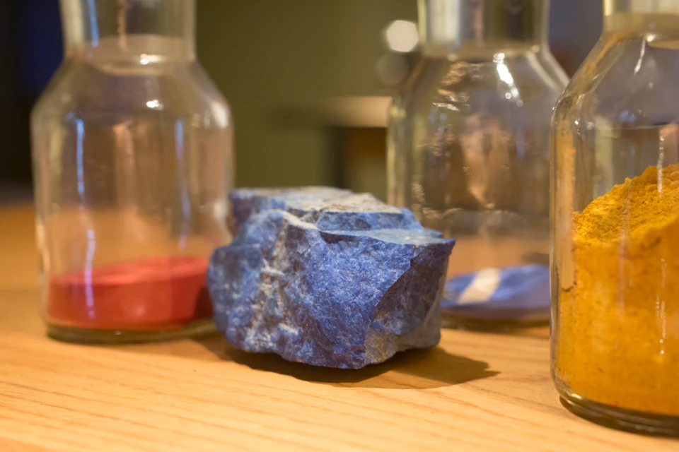 A rough blue stone placed on a wooden surface surrounded by three clear glass bottles.
