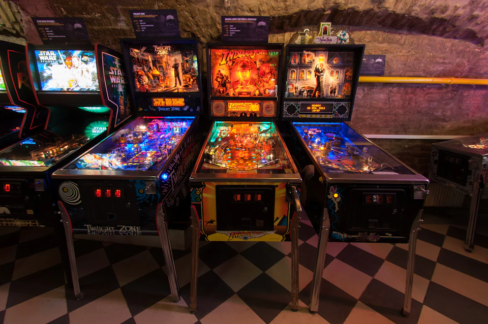 Three pinball machines with vibrant, illuminated playfields themed after Twilight Zone, Indiana Jones, and The Addams Family.