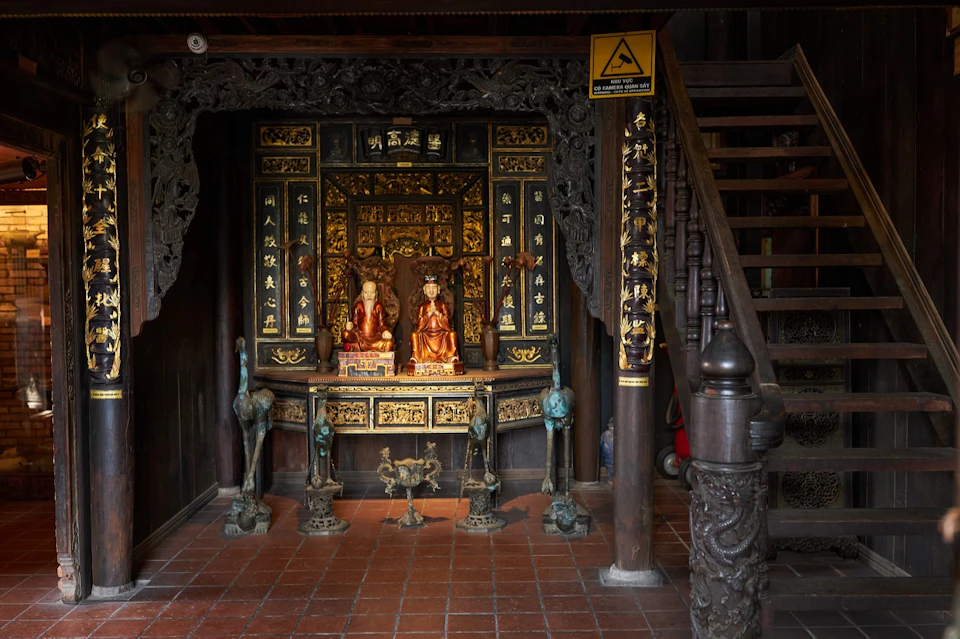 An ornate altar with golden decorations and statues, surrounded by carved wood and intricate details, next to a wooden staircase.