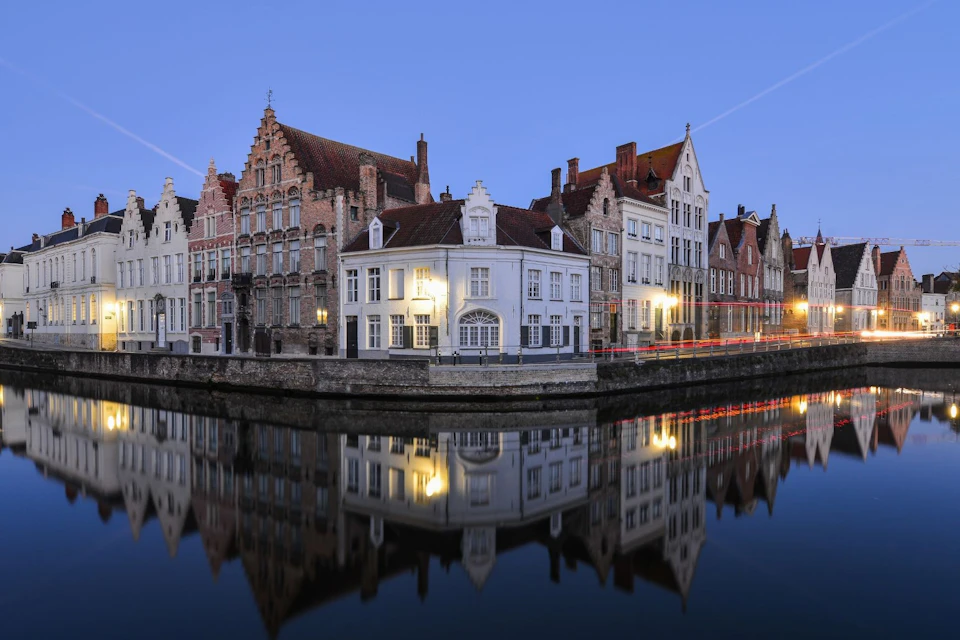 Canal-side European buildings with ornate facades and gabled roofs reflected in the calm water under a twilight sky.