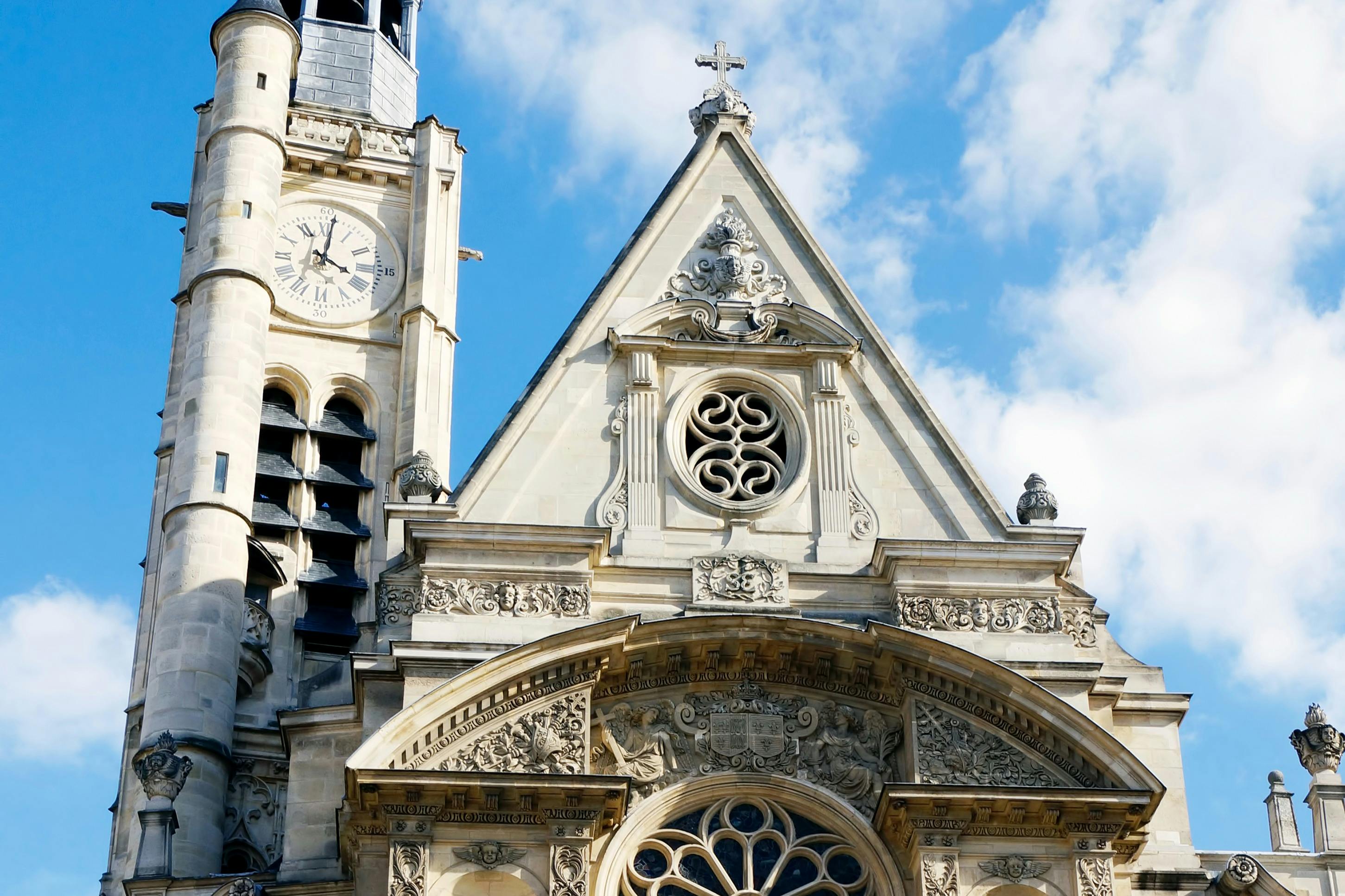 哥特式教堂立面上有华丽的雕刻、钟楼、玫瑰窗，在蓝色的天空下穿过，云层很少。