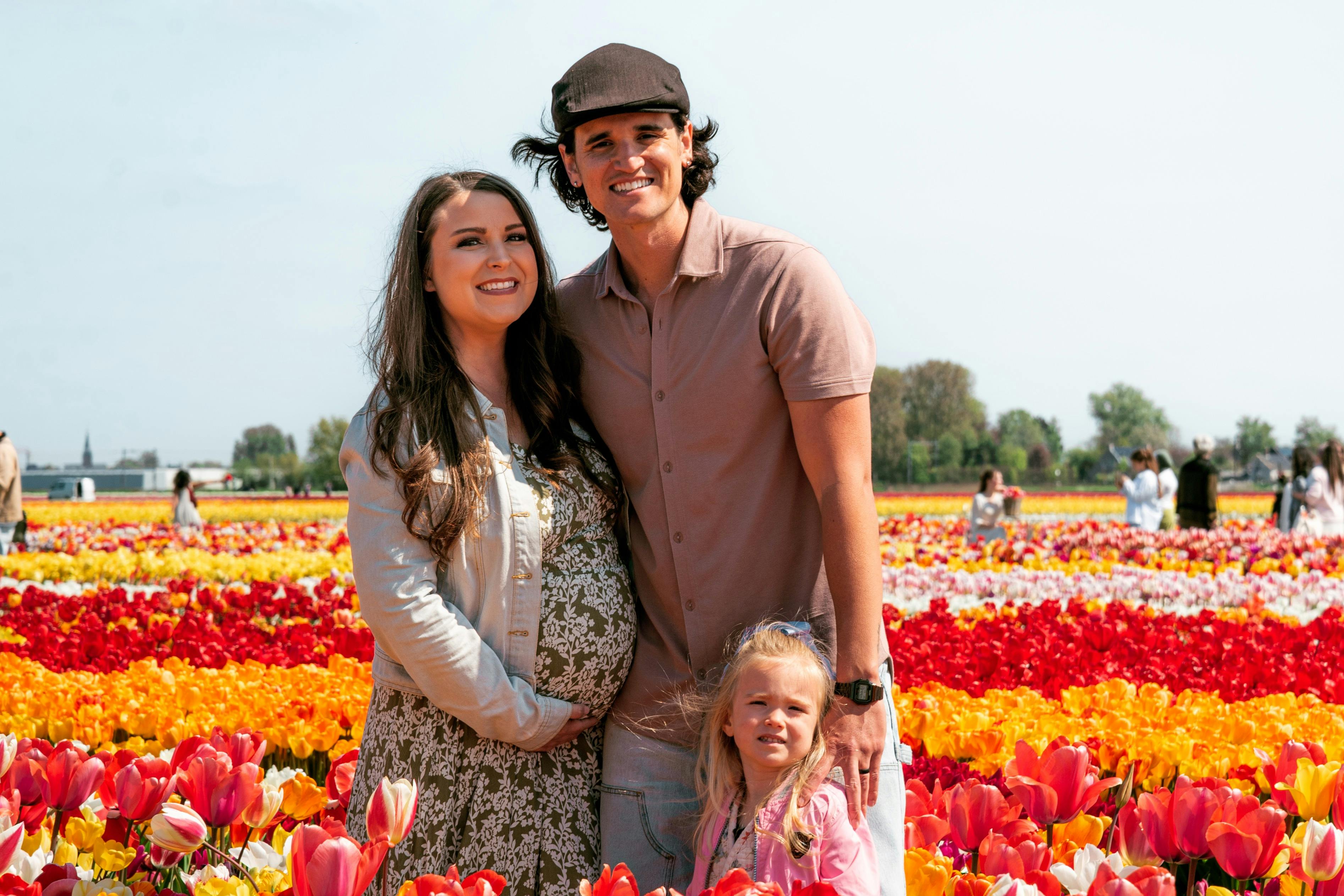 A smiling couple and a child stand in a colourful tulip field under a clear sky.