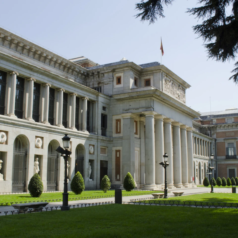 Large neoclassical building with tall columns and arched windows, surrounded by a well-manicured lawn and lampposts.