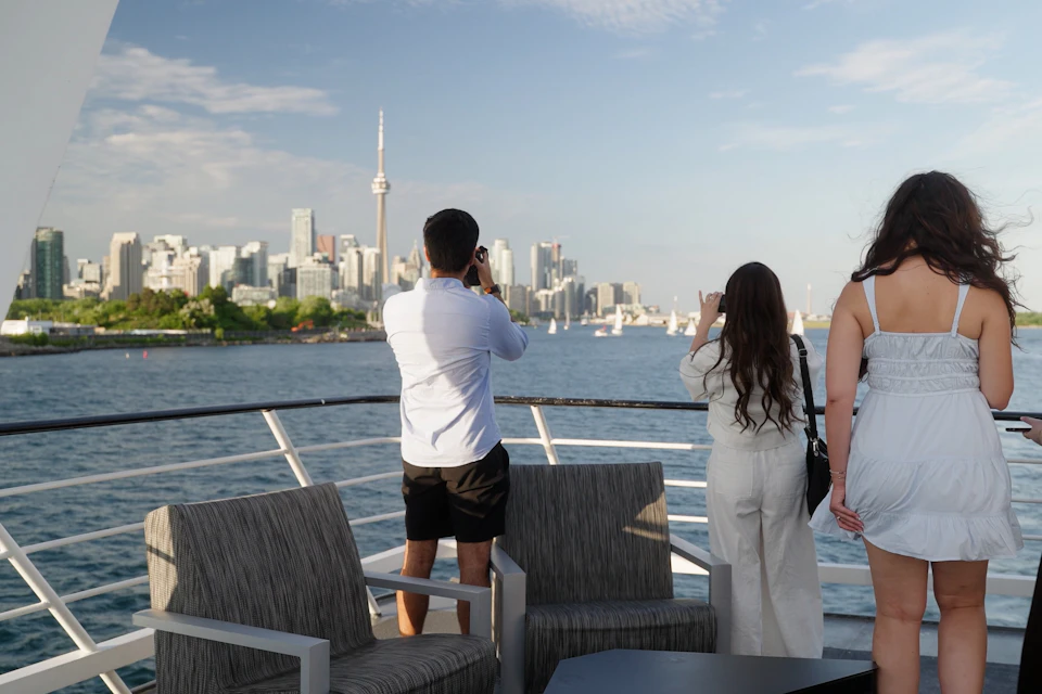 People on a boat deck taking photos of a city skyline with a prominent tower, under a blue sky.