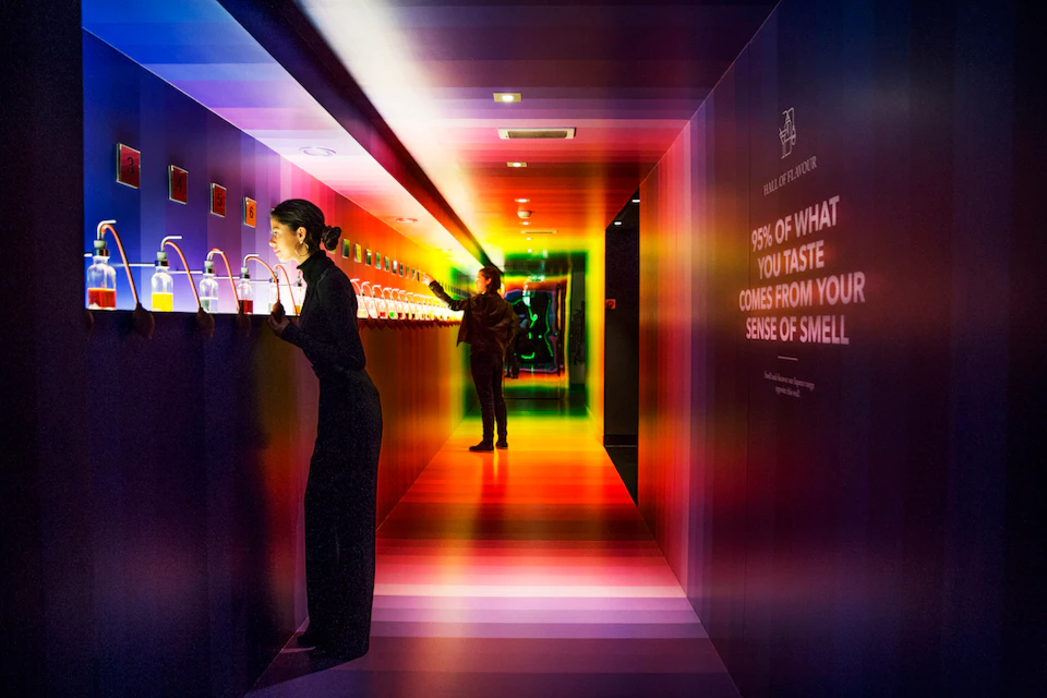 Two people in a multicolored tunnel inspecting an interactive display with jars. Text on the wall reads, "95% of what you taste comes from your sense of smell."