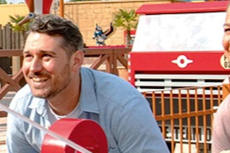 A family operates a fire truck-themed attraction in an outdoor amusement park on a sunny day.