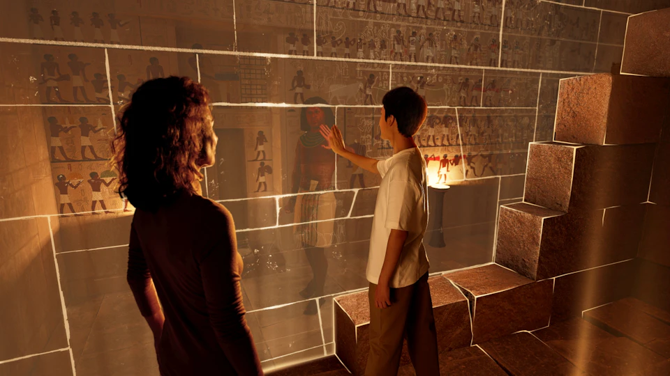 Two people observe ancient Egyptian wall etchings behind a glass display, with one person touching the glass.