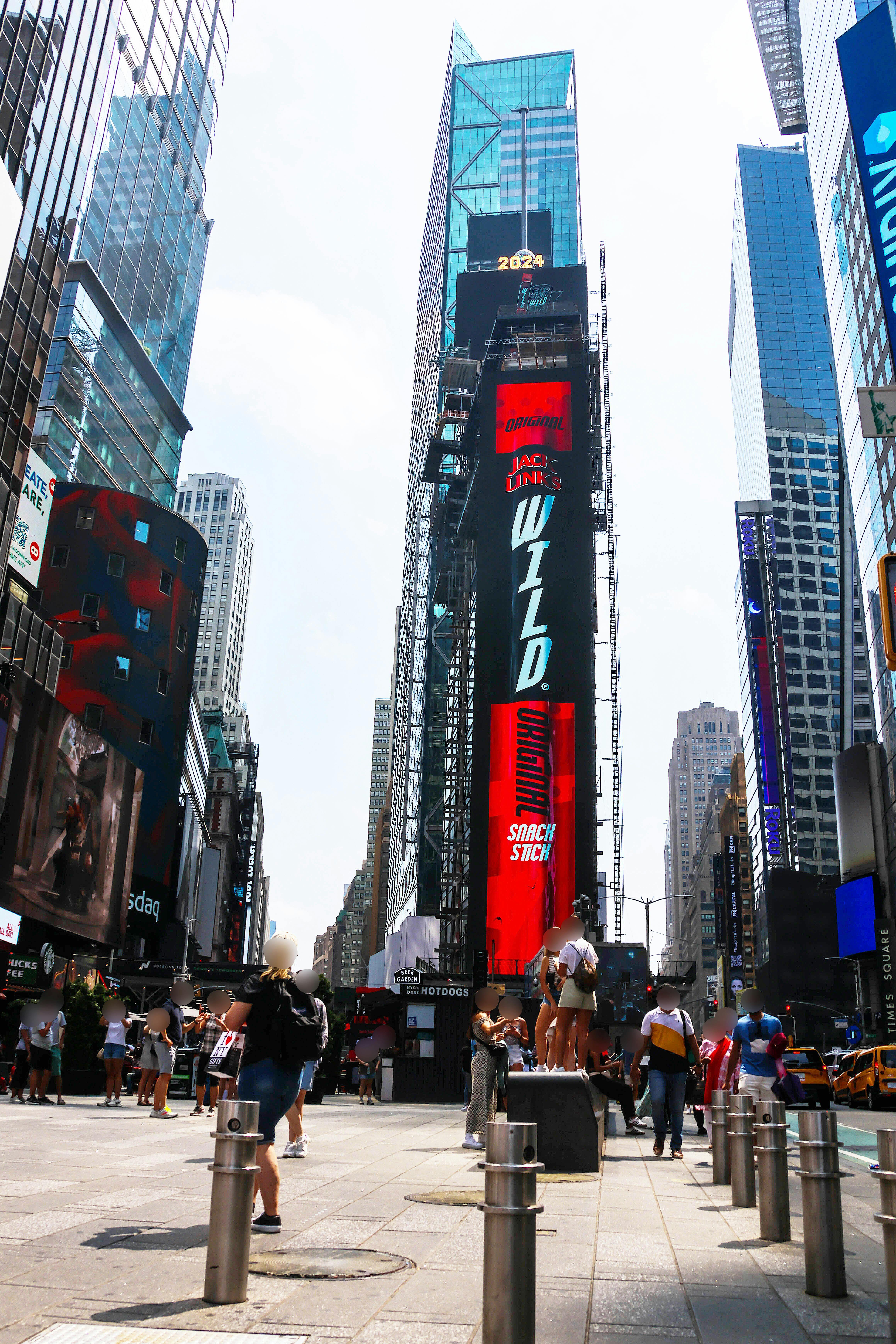 Crowd of people walking in Times Square, New York, surrounded by tall buildings and large digital billboards.