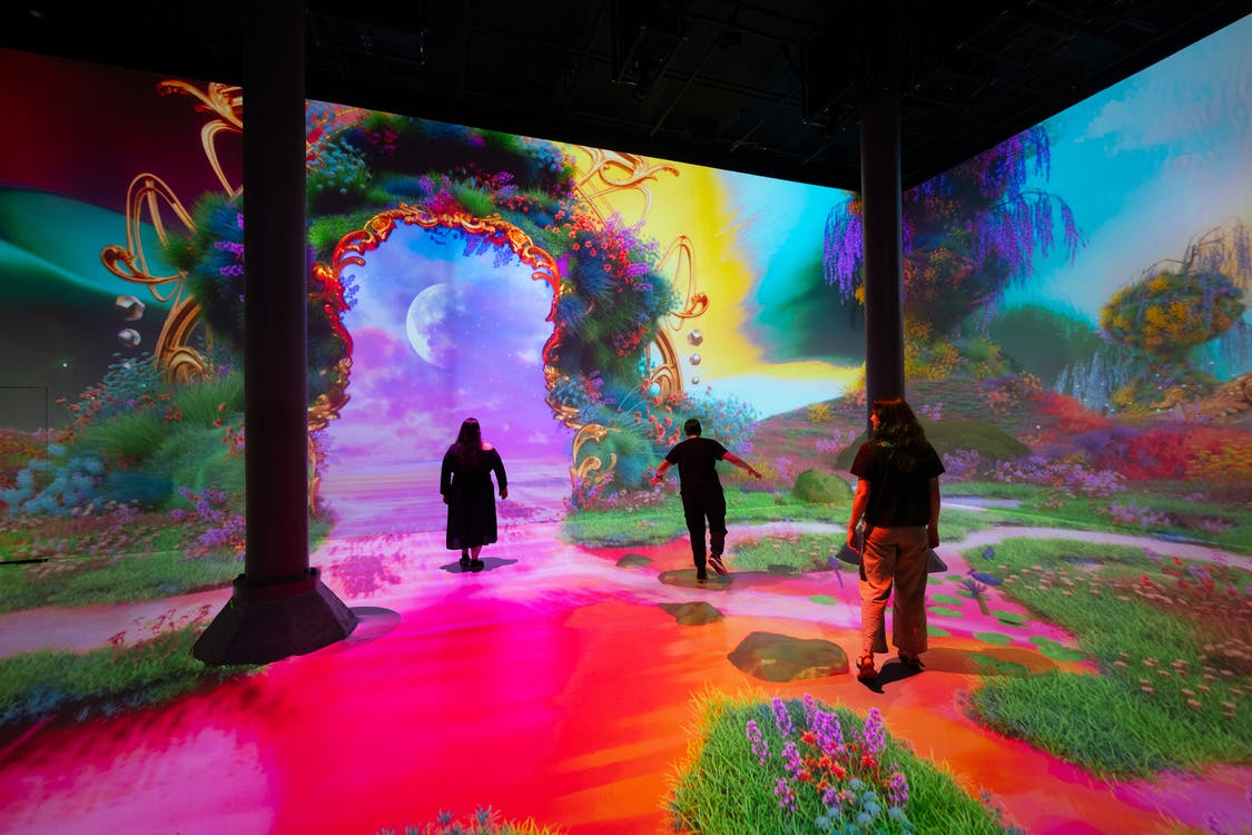 Menschen, die durch eine farbenfrohe, immersive digitale Kunstinstallation mit einem gewölbten Portal und einer lebendigen Szenerie gehen.