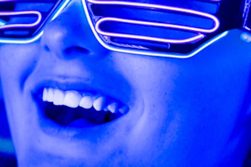 Two women wearing glowing glasses in a neon-lit environment, smiling and enjoying the vibrant atmosphere.