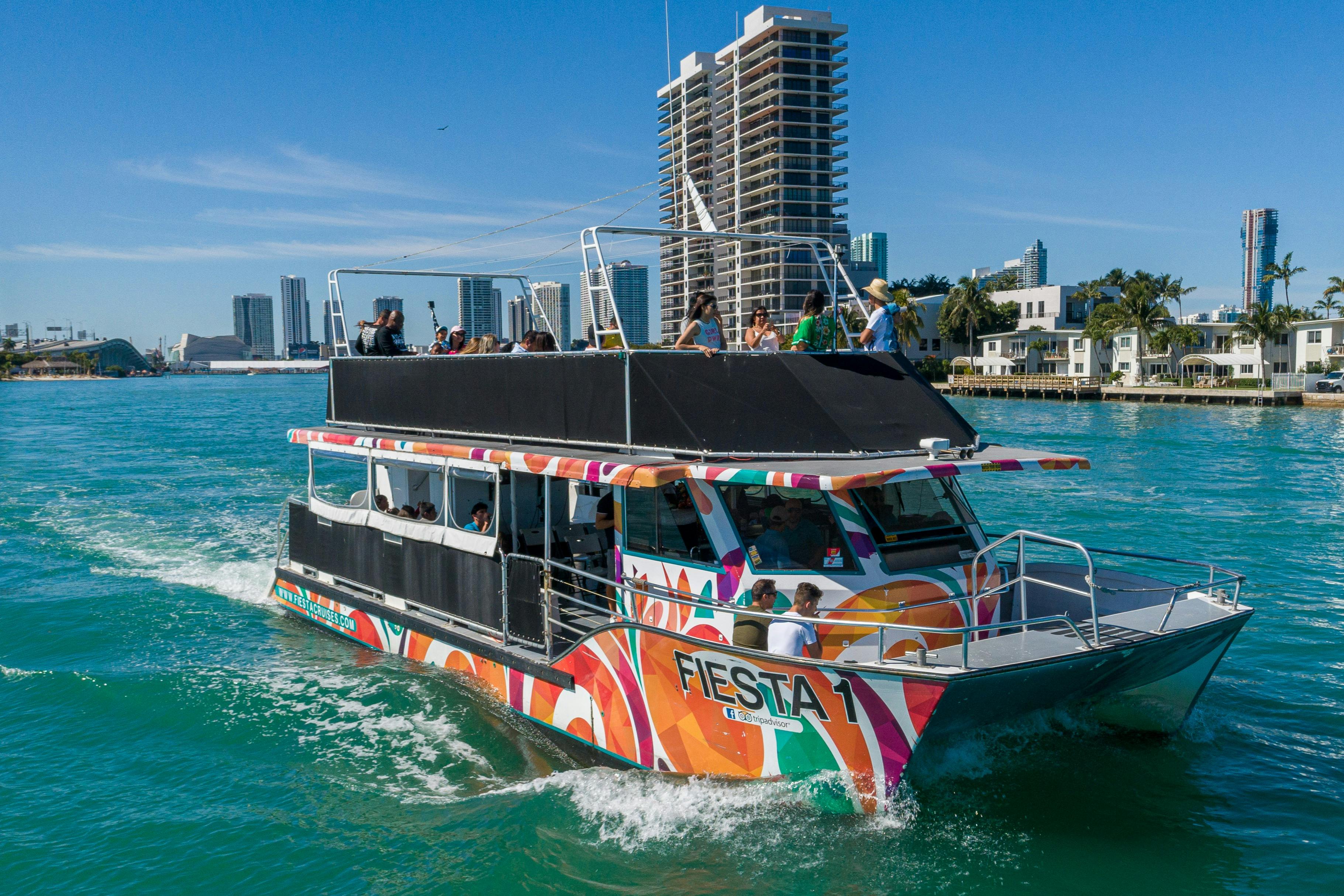 A colorful boat named 'Fiesta 1' on water with passengers aboard, against a backdrop of modern buildings and a blue sky.