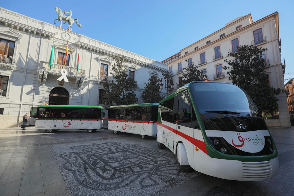Three green and white buses parked in front of a historic building with a large white ribbon on the facade.