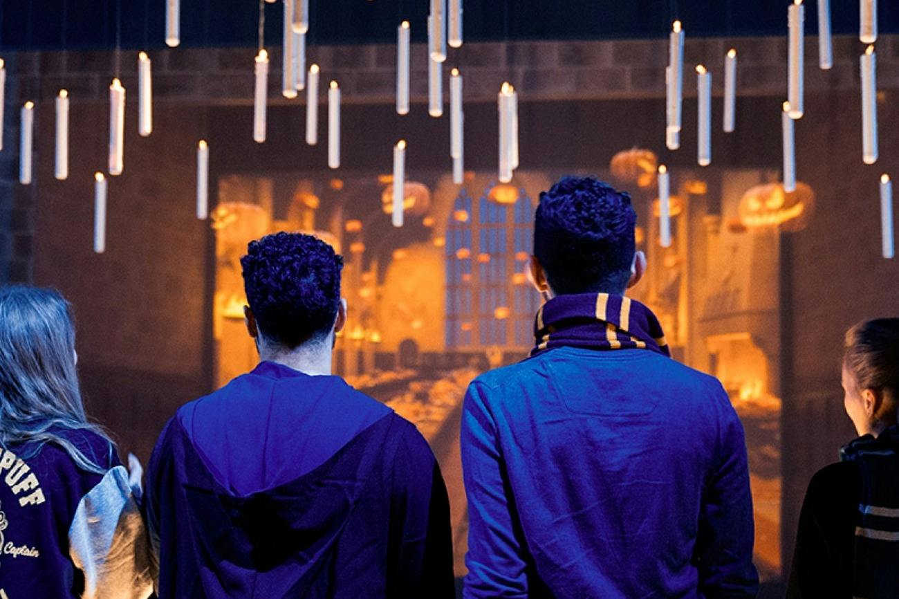 Two people with curly hair, seen from behind, facing a room with floating candles and a warm, glowing ambiance.