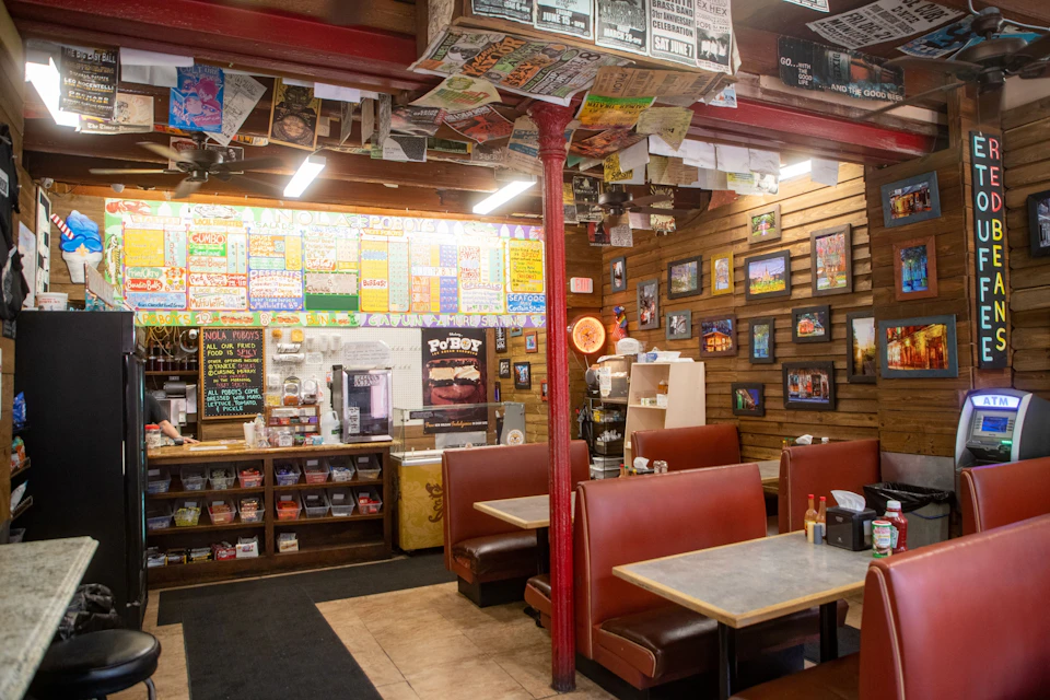 A cozy diner interior with colorful menu boards, framed pictures on wooden walls, and red booth seating with tables.