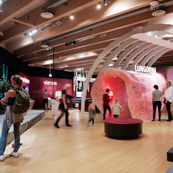 Museiutställning med interaktiva skärmar; människor som utforskar en stor, genomgångsmodell av lungor. Takbelysning och informationspaneler.