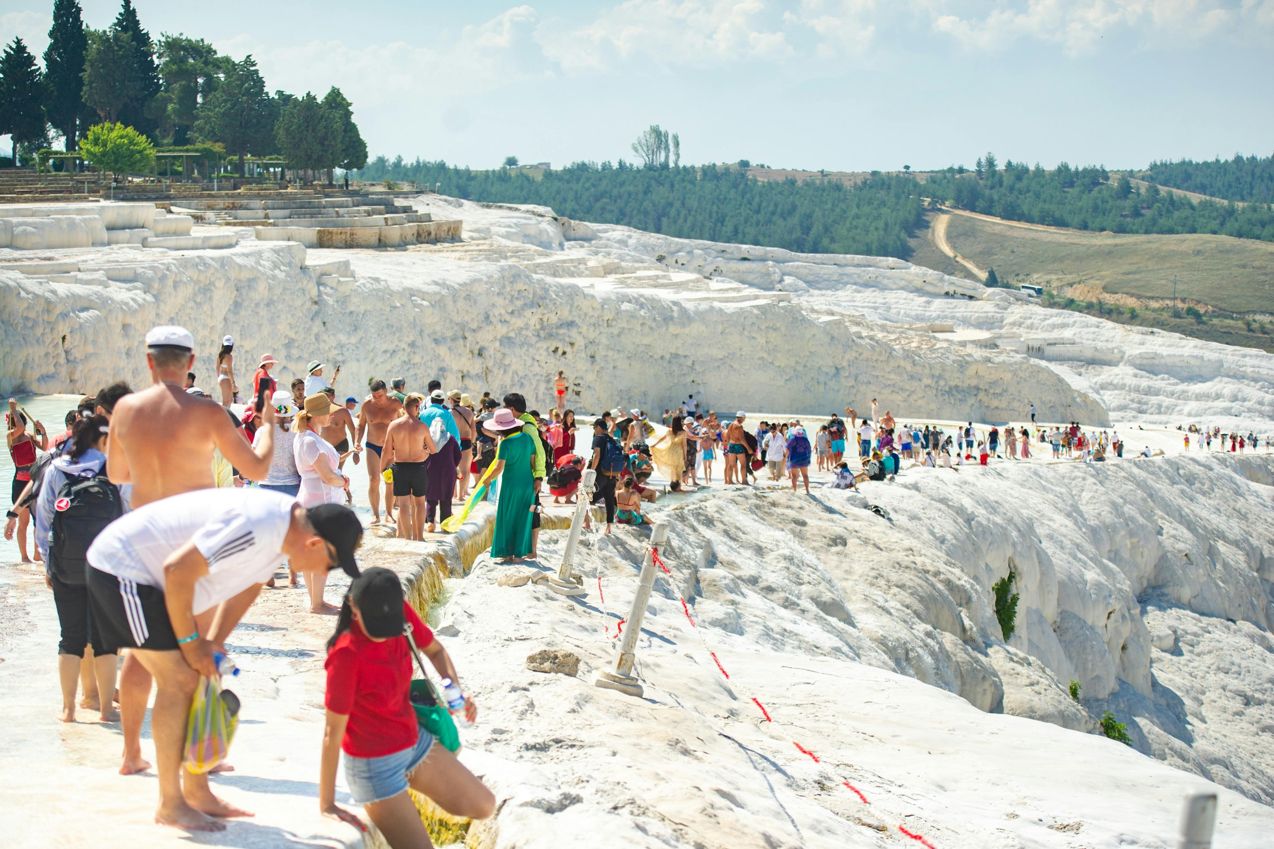 Crowd of tourists walking on a white, rocky landscape with people lounging and enjoying the scenery, greenery in the background.