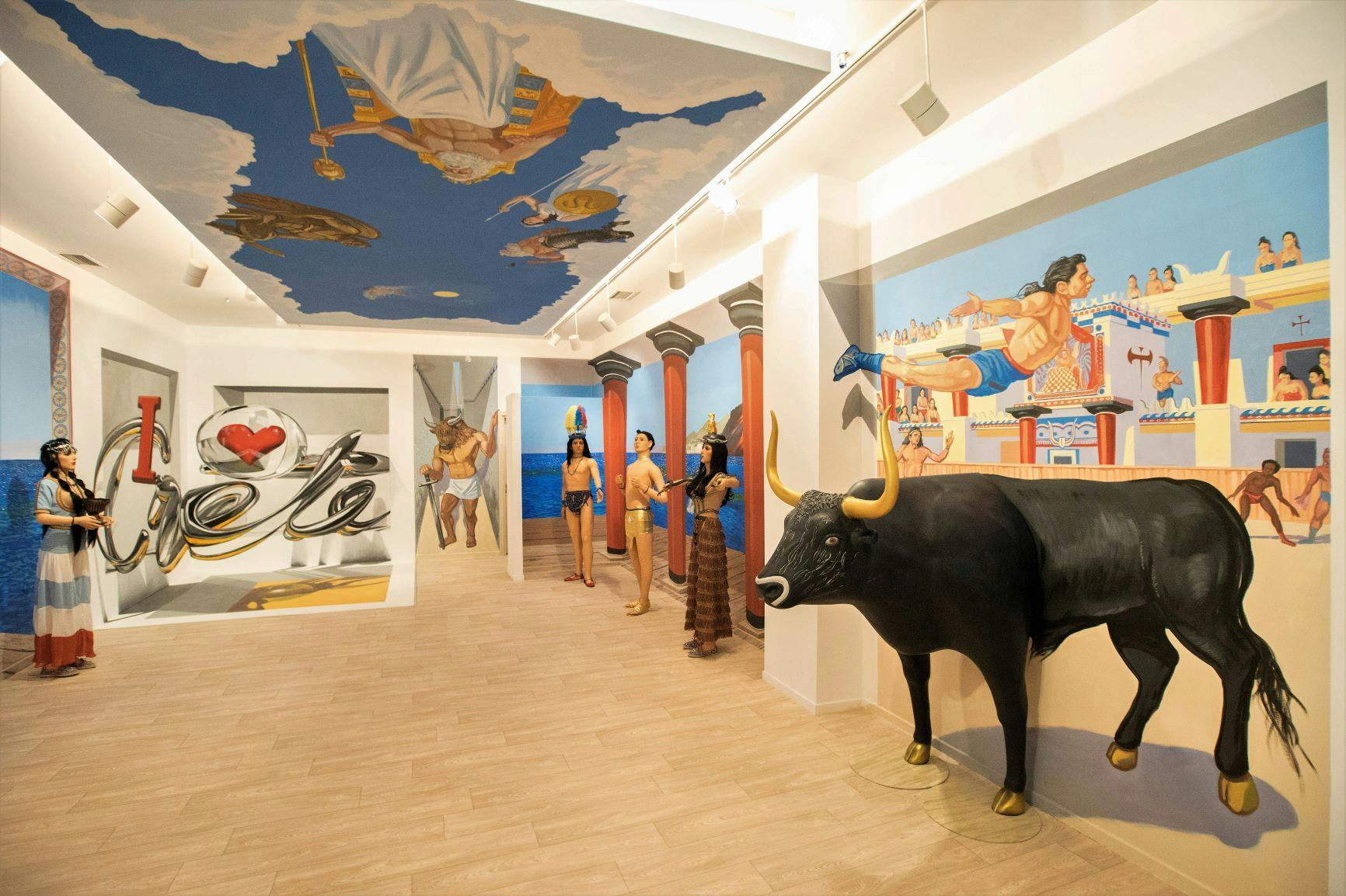 Expozice muzea se sochami řecké mytologie v životní velikosti, černým býkem a stropním uměním zobrazujícím bohy proti zamračené obloze.