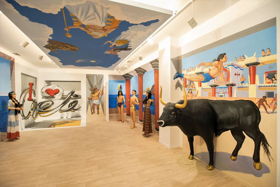 Museum exhibit with life-sized Greek mythology statues, a black bull, and ceiling art depicting gods against a cloudy sky.