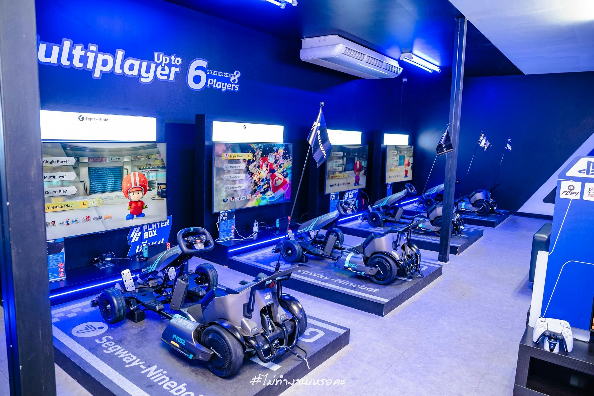 A gaming setup featuring Segway-Ninebot vehicles and screens displaying a racing game in a blue-lit room for up to six players.