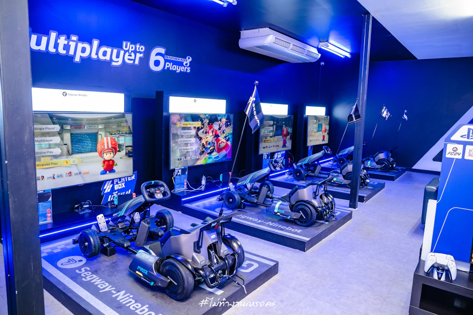 A gaming setup featuring Segway-Ninebot vehicles and screens displaying a racing game in a blue-lit room for up to six players.