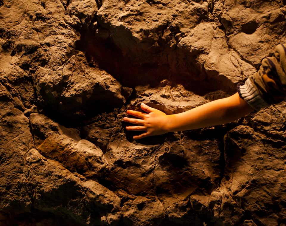 A child's hand touches a textured, rocky surface in warm lighting.
