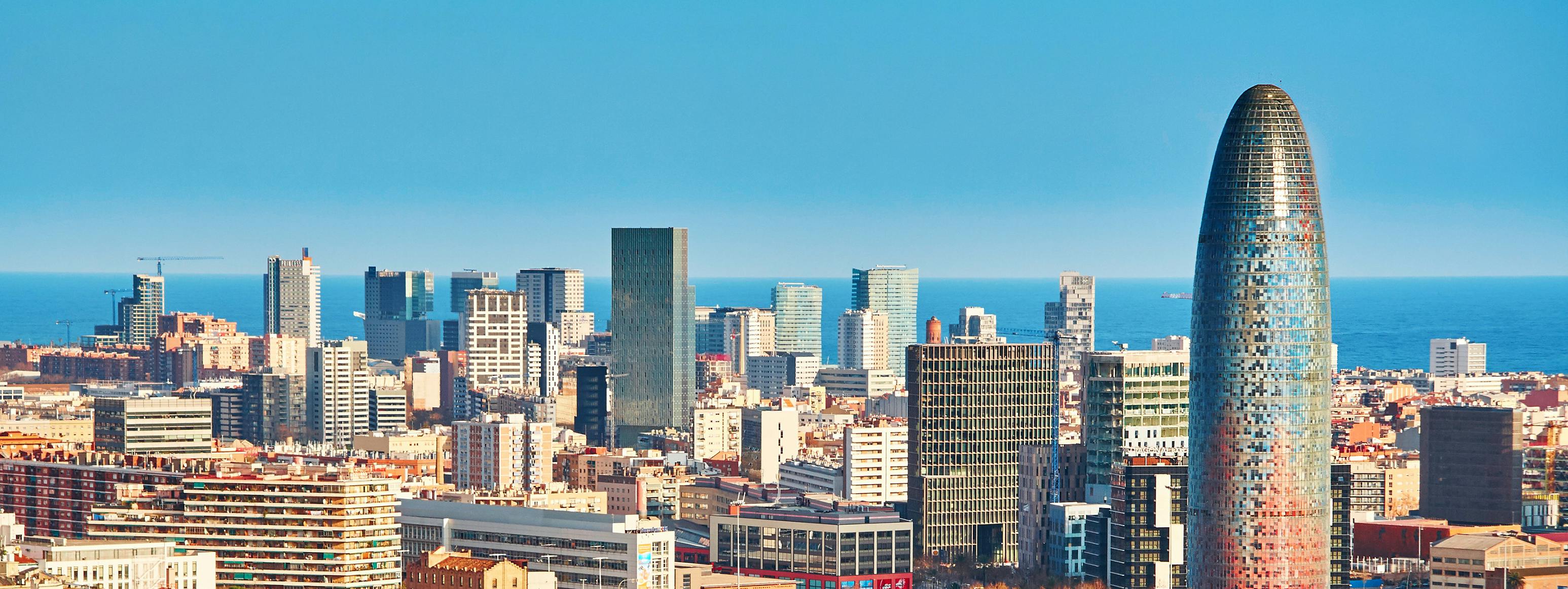 Un paysage urbain composé de gratte-ciel modernes et de bâtiments plus anciens, avec un horizon océanique et un ciel bleu en arrière-plan.