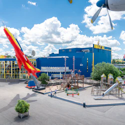 Museets entré med en färgglad flygplansskärm, IMAX 3D-teater och en närliggande lekplats under en blå himmel med moln.