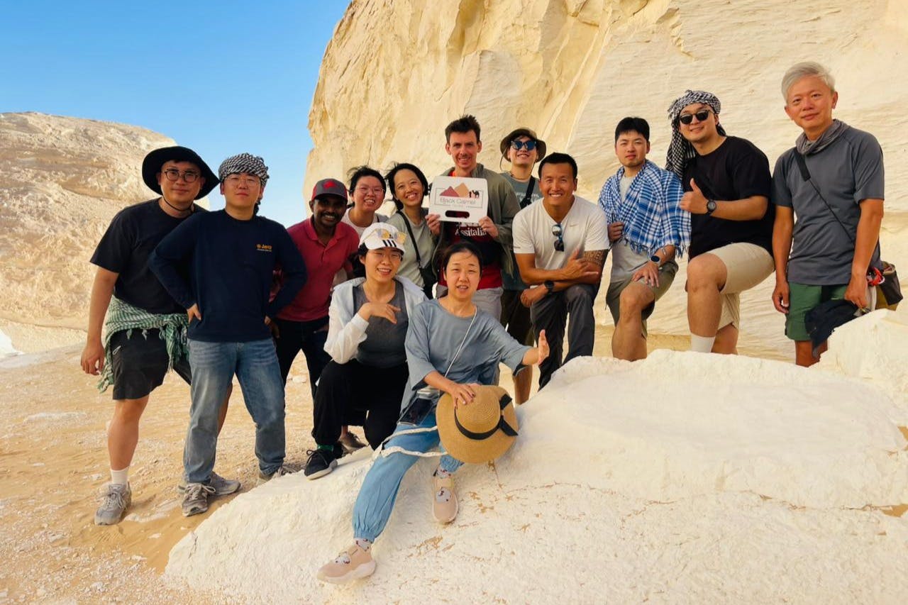 A group of people posing on a white rock formation under a clear blue sky, some wearing hats and sunglasses, smiling for the camera.